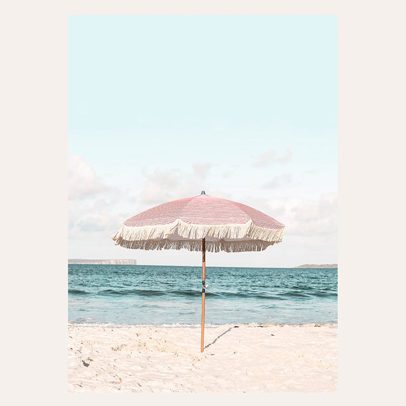 a pink and white umbrella sitting on top of a sandy beach