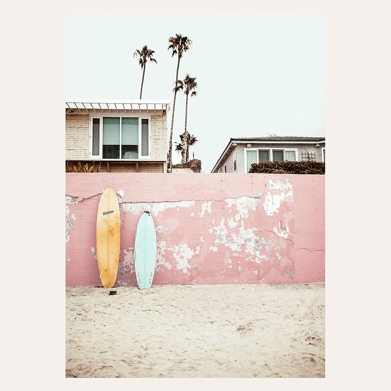 two surfboards leaning against a pink wall on a beach